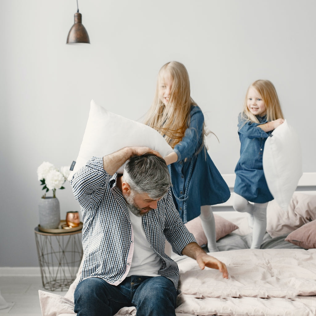 Father and kids enjoying a pillow fight on DLX mattress with commitment to low pricing