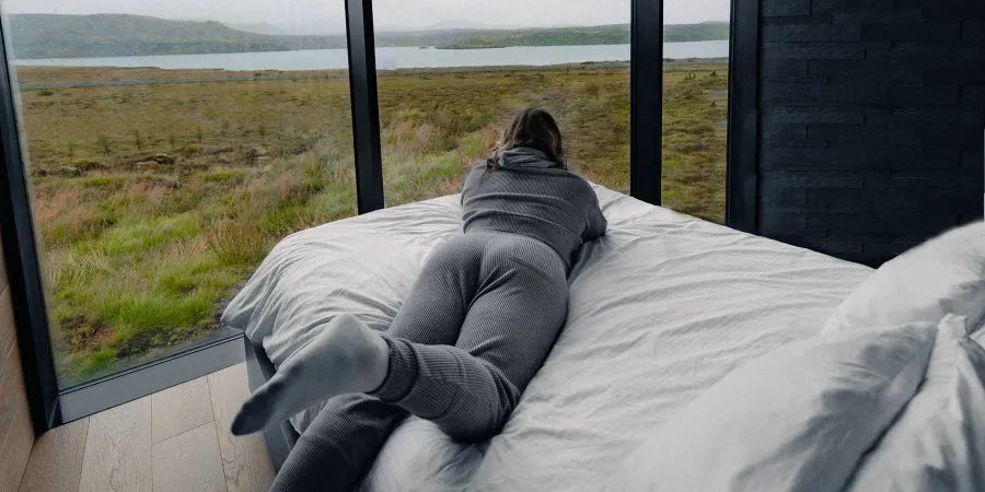 A woman peacefully lying in bed looking out the window, symbolizing good sleep habits.