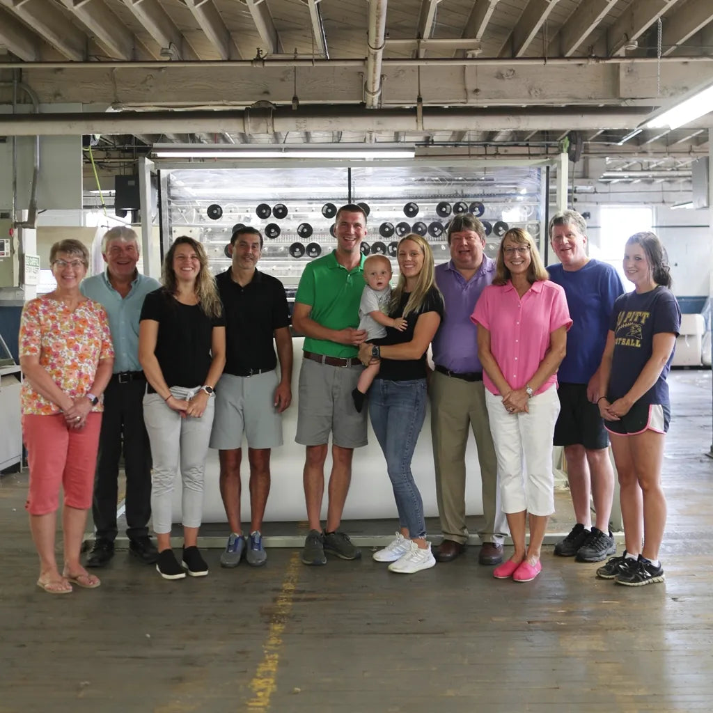 The Pullan family posing in front of a quilter at their mattress factory in New York, showing all generations of the family.