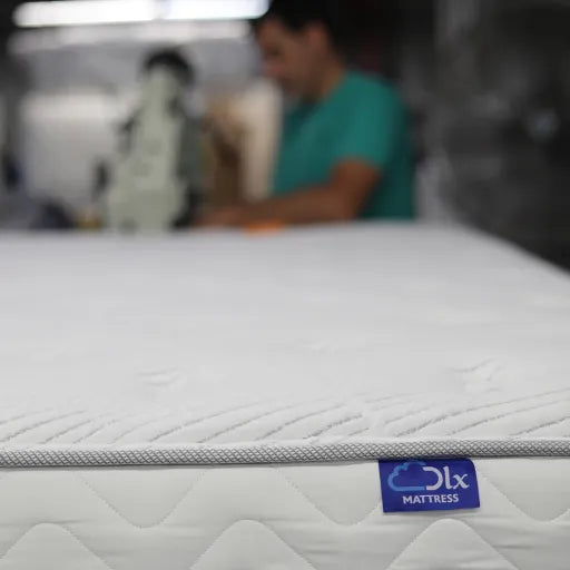 Craftsperson meticulously sewing a DLX Mattress with its signature blue logo label.