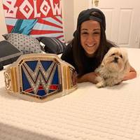 WWE's Bayley resting on a DLX mattress, proudly displaying her championship belt.