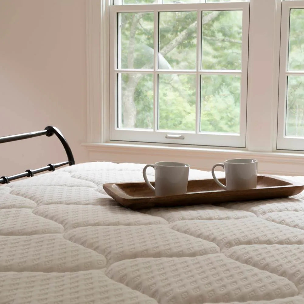 A serene morning scene with coffee on DLX mattress in the backdrop of a window, directing to the FAQ section for warranty.
