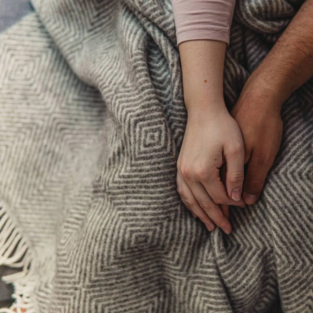 Couple's hands intertwined atop a warm blanket. Emphasizing the hope and security DLX's Giving Back initiative provides.
