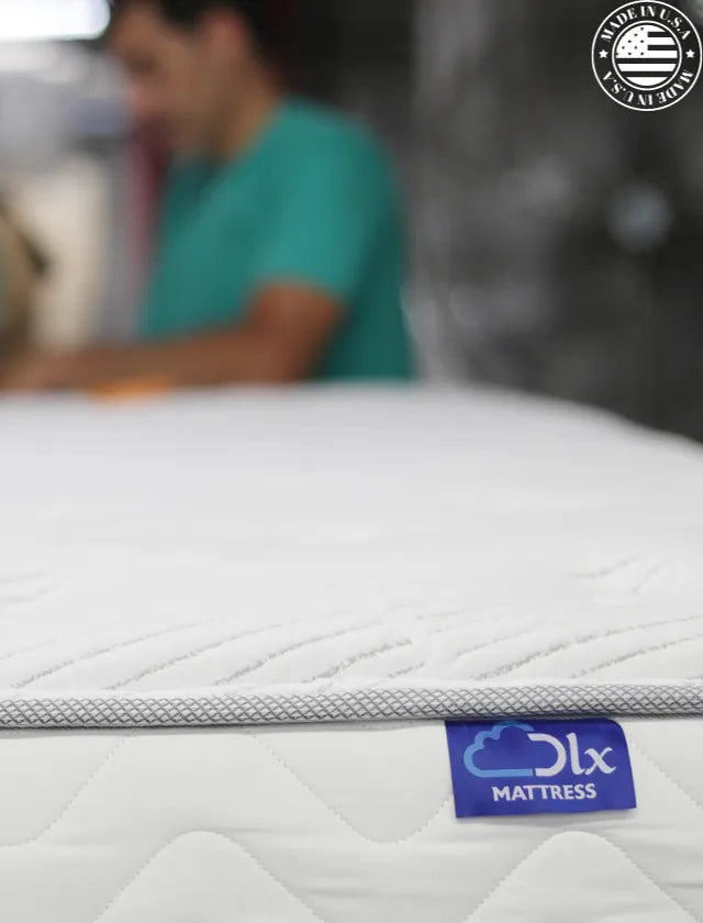 Mattress being tape edged, displaying the blue DLX label and 'Made in the USA' logo